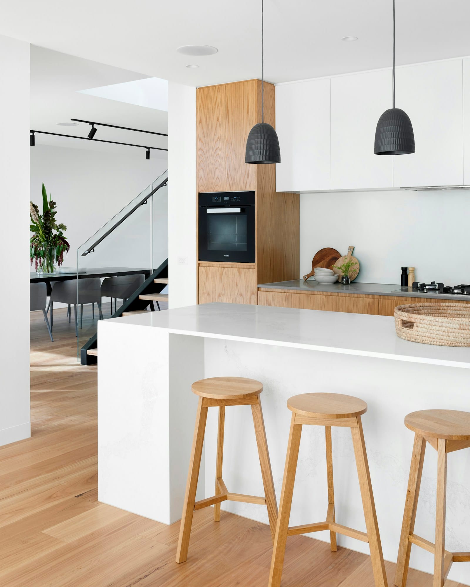 A kitchen island in pale stone and timber with three stools and a staircase behind